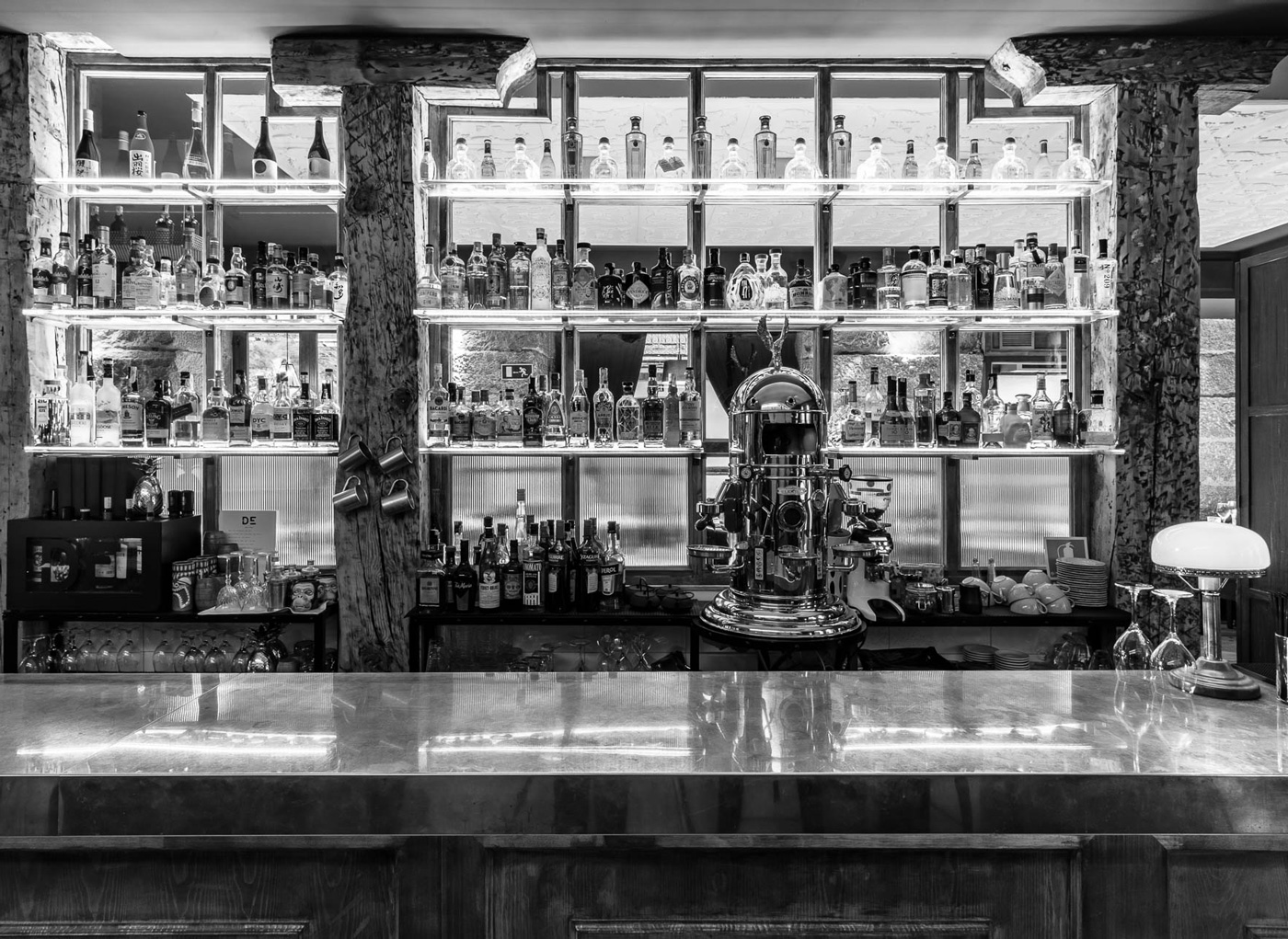 Vista de la barra de un bar con bebidas y botellas al fondo.